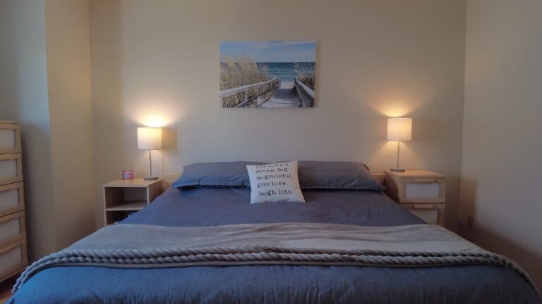 Mala spavaća soba sa jednostavnim nameštajem, dve stojeće lampe i slikom iznad kreveta