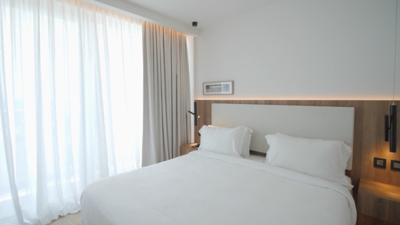 Mala spavaća soba sa velikim prozorima, belom posteljinom i diskretnom rasvetom