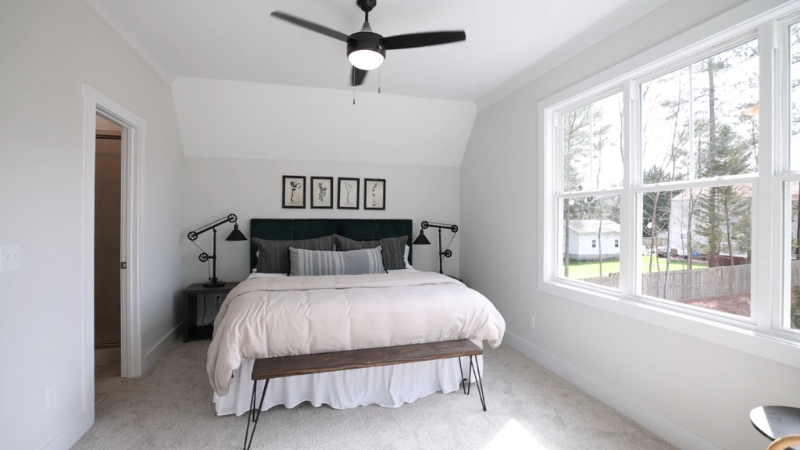 Mala spavaća soba sa krevetom i klupicom na nogama, velikim prozorom i svetlim zidovima