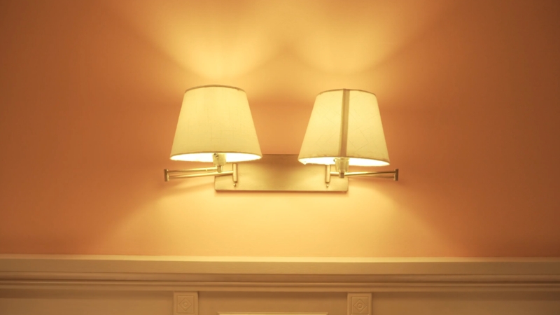 Dve zidne lampe sa toplim svetlom na nežno obojenom zidu